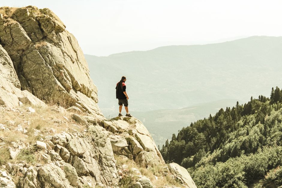 A lone hiker stands on a rocky cliff overlooking lush mountains in Bursa, Türkiye.