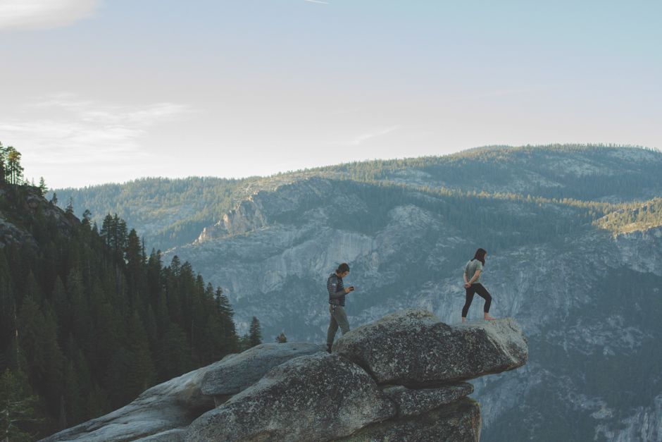 Two people standing on a cliff edge surrounded by stunning mountain scenery.